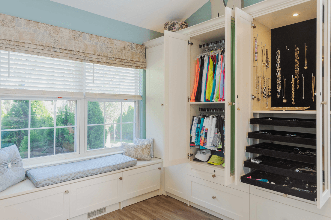 Custom closet designed around a window with built-in seating, cabinetry, and jewelry storage.